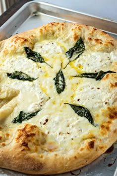 a pizza with cheese and spinach leaves on it sitting in a metal pan next to a window