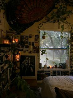 a bedroom with lots of plants and pictures on the wall next to the bed in front of the window