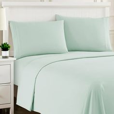 a bed with light green sheets and pillows on top of it, next to a night stand