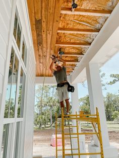 a man on a ladder painting the roof of a house with wood planks and paint