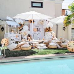 an outdoor dessert table set up by the pool with white umbrellas and cookies on it