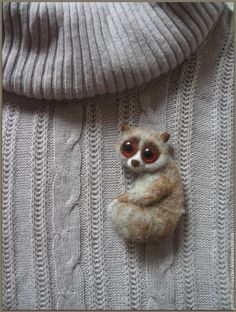 a small stuffed animal sitting on top of a gray sweater with eyes wide open and one eye partially closed