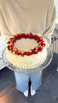 a person holding a cake with strawberries on top