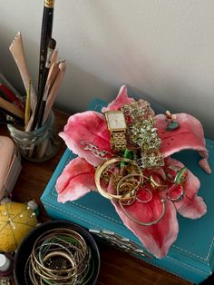 an arrangement of jewelry sits on top of a blue box next to pens and pencils