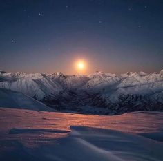 the sun is setting over snowy mountains with snow covered ground and stars in the sky