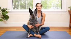 a woman sitting on a yoga mat holding a dog