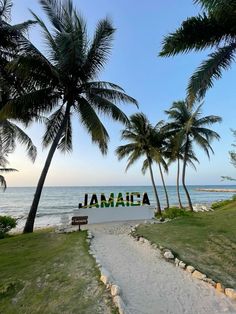 there is a sign that says jamaica on the beach with palm trees in the foreground