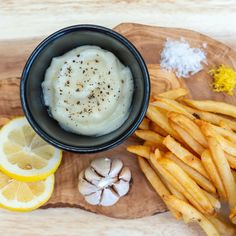 a wooden cutting board topped with french fries and a bowl filled with mashed potatoes