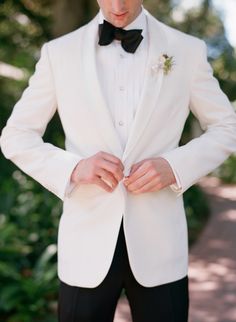 a man in a white tuxedo and black bow tie is holding his jacket open