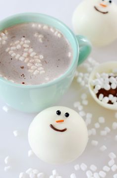 two marshmallows are next to a cup of hot chocolate and some marshmallows