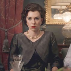 a woman sitting at a table with a glass in front of her and another person standing behind her