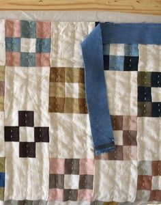 an old quilt is laying on the floor next to a pair of blue jeans and a wooden table