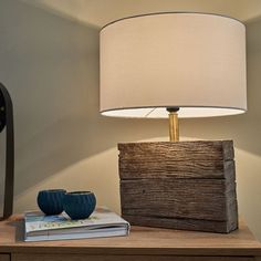 a lamp sitting on top of a wooden table next to a book and a vase