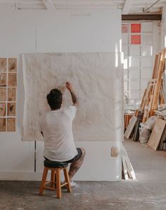 a man sitting on a stool in front of a large piece of art that is being worked on