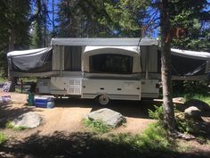 an rv is parked in the woods near some rocks and trees with tarps on it