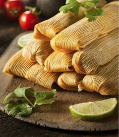 tamales stacked on top of each other with limes and tomatoes in the background