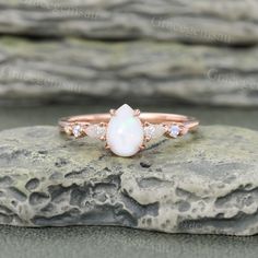 a white opal and diamond ring sitting on top of a rock