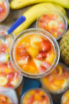 there are many small cups with fruit in them on the table next to bananas and pineapples