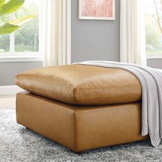 a tan leather ottoman sitting on top of a gray rug in front of a window