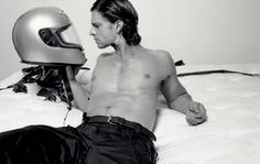 a shirtless man laying on top of a bed with a motorcycle helmet in his hand