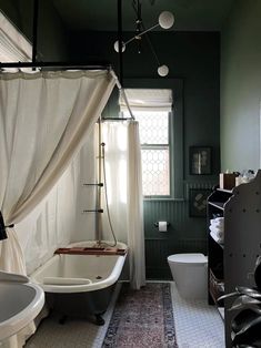 an old fashioned bathtub and sink in a bathroom with dark green walls, carpeted flooring and white curtains