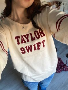 a woman wearing a sweater with the word taylor swift on it, and holding her arms behind her head