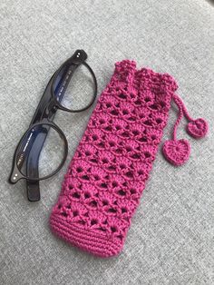 a pink crocheted cell phone case next to glasses on a gray surface with a pair of eyeglasses