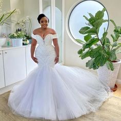 a woman in a white wedding dress standing next to a potted plant and looking at the camera