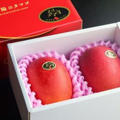 two red apples sitting in a box on a table next to an orange box with chinese writing