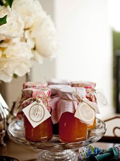 jars filled with jam sitting on top of a glass platter next to white flowers