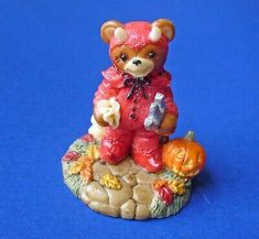 a small figurine of a teddy bear holding a pumpkin on a blue background