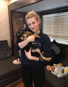 a woman is holding two small dogs in her arms while standing next to a couch