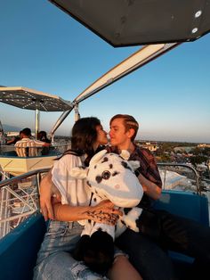 two people sitting on a boat kissing and holding stuffed animals in their hands while the sun is setting