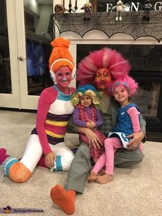 three children in costumes sitting on the floor next to a fireplace with their faces painted pink and orange