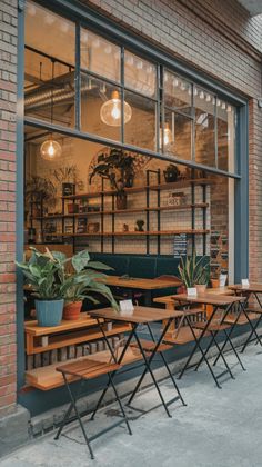 tables and chairs are lined up in front of a store window with potted plants