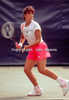 a woman in pink shorts and white shirt playing tennis on a court with a racket