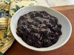 a white bowl filled with blueberries sitting on top of a wooden table next to a yellow towel