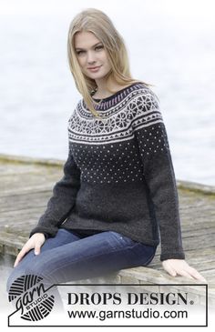 a woman is sitting on a dock wearing a sweater and jeans with her legs crossed