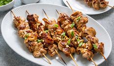 chicken skewers on a plate with chopsticks next to bowls of greens