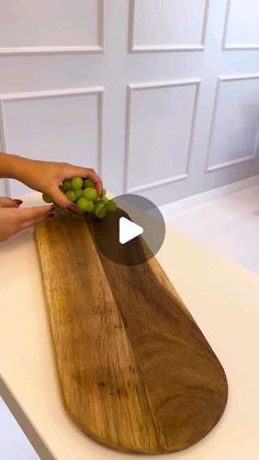 a person is cutting grapes on a wooden board with a video screen showing how to use it