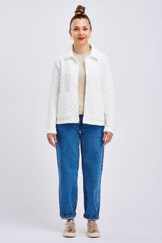 a woman standing in front of a white background wearing blue jeans and a white jacket