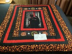 a bed with a black and red quilt on it's side, featuring an image of a man holding a bat