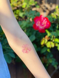 a person's arm with a flower on it and a red rose in the background