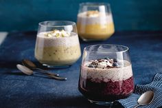 three desserts in glasses on a table with spoons