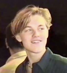 a young man with blonde hair wearing a green shirt and yellow tie smiling at the camera