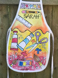 a child's apron with the word sarah painted on it, hanging from a wooden fence