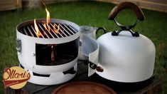 a white kettle sitting on top of a wooden table next to a grill with flames