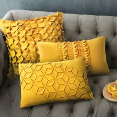 a gray couch with yellow pillows and orange slices on it, next to a glass of orange juice