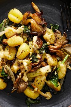 a black plate topped with potatoes and greens next to a fork on a tablecloth