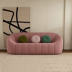 a pink couch sitting on top of a rug in front of a wall mounted painting